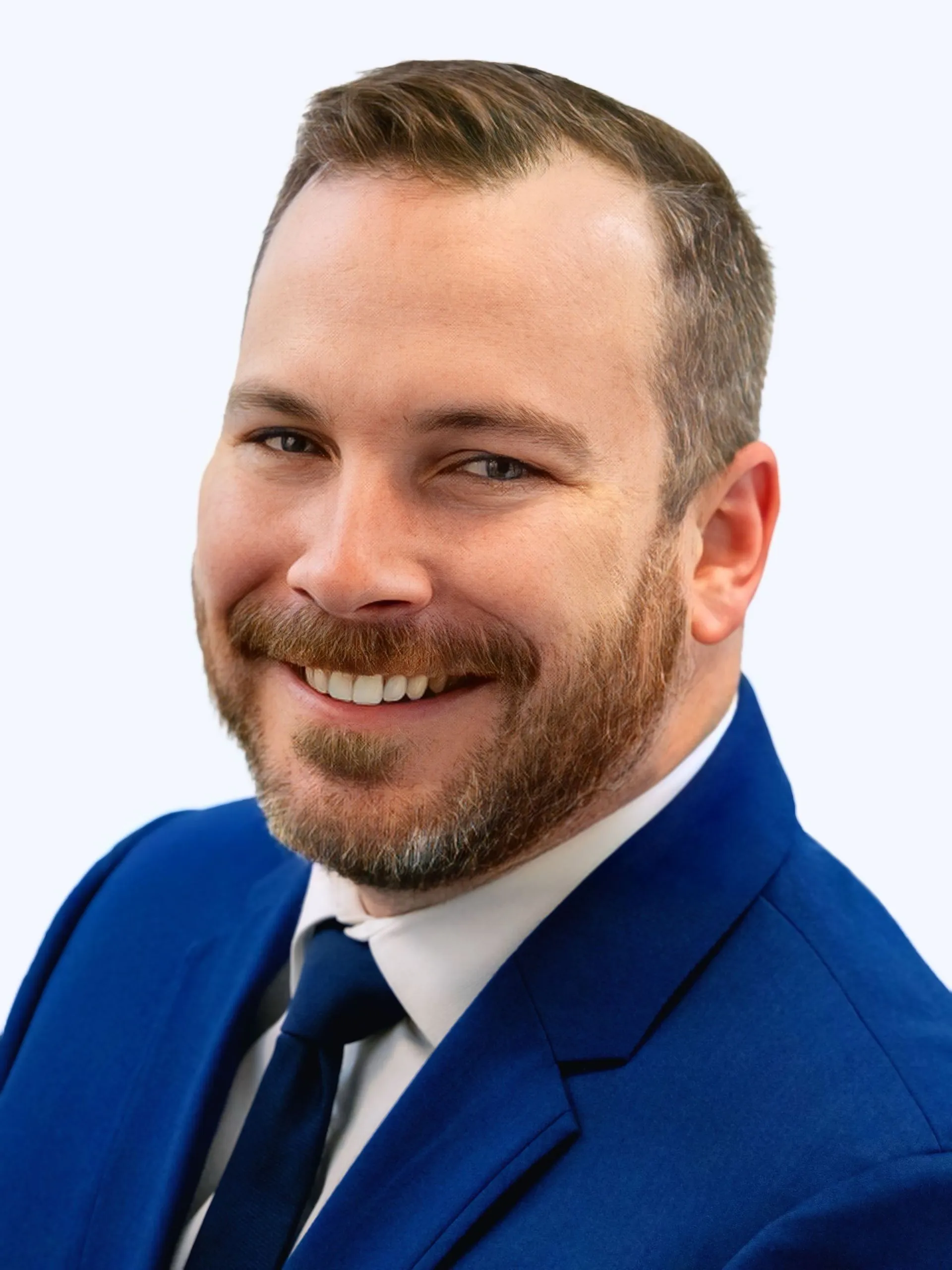 Portrait of a smiling man with a beard wearing a blue suit and tie against a light background.