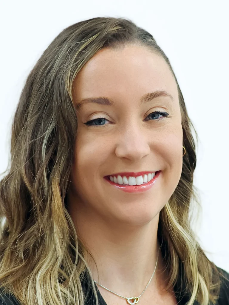Professional headshot of a smiling woman with wavy blonde hair and blue eyes against a white background.