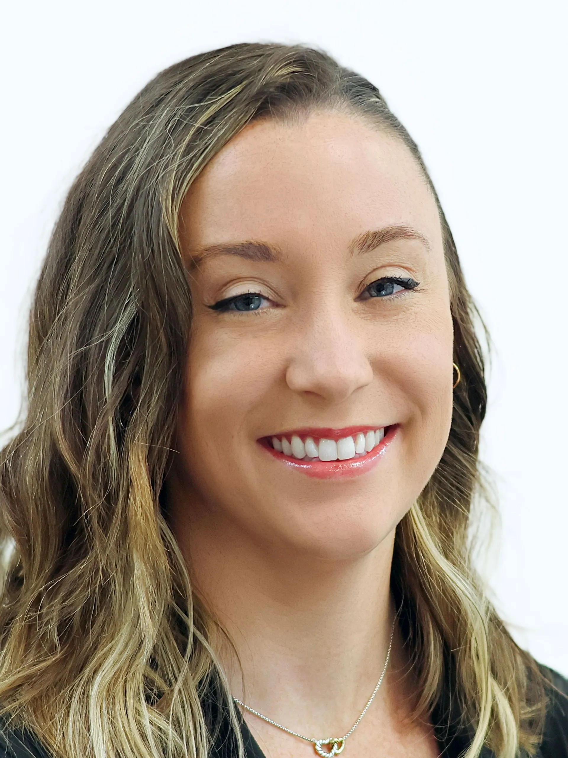 Professional headshot of a smiling woman with wavy blonde hair and blue eyes against a white background.