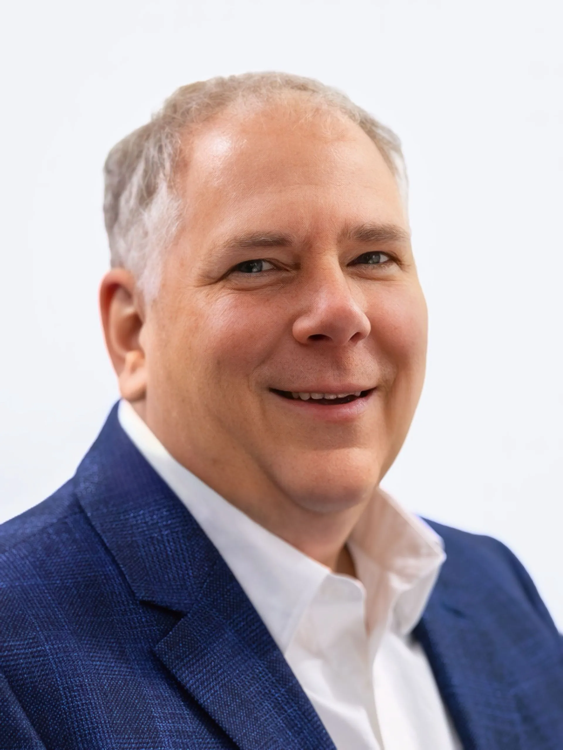 Professional headshot of a middle-aged man in a blue blazer and white shirt smiling.