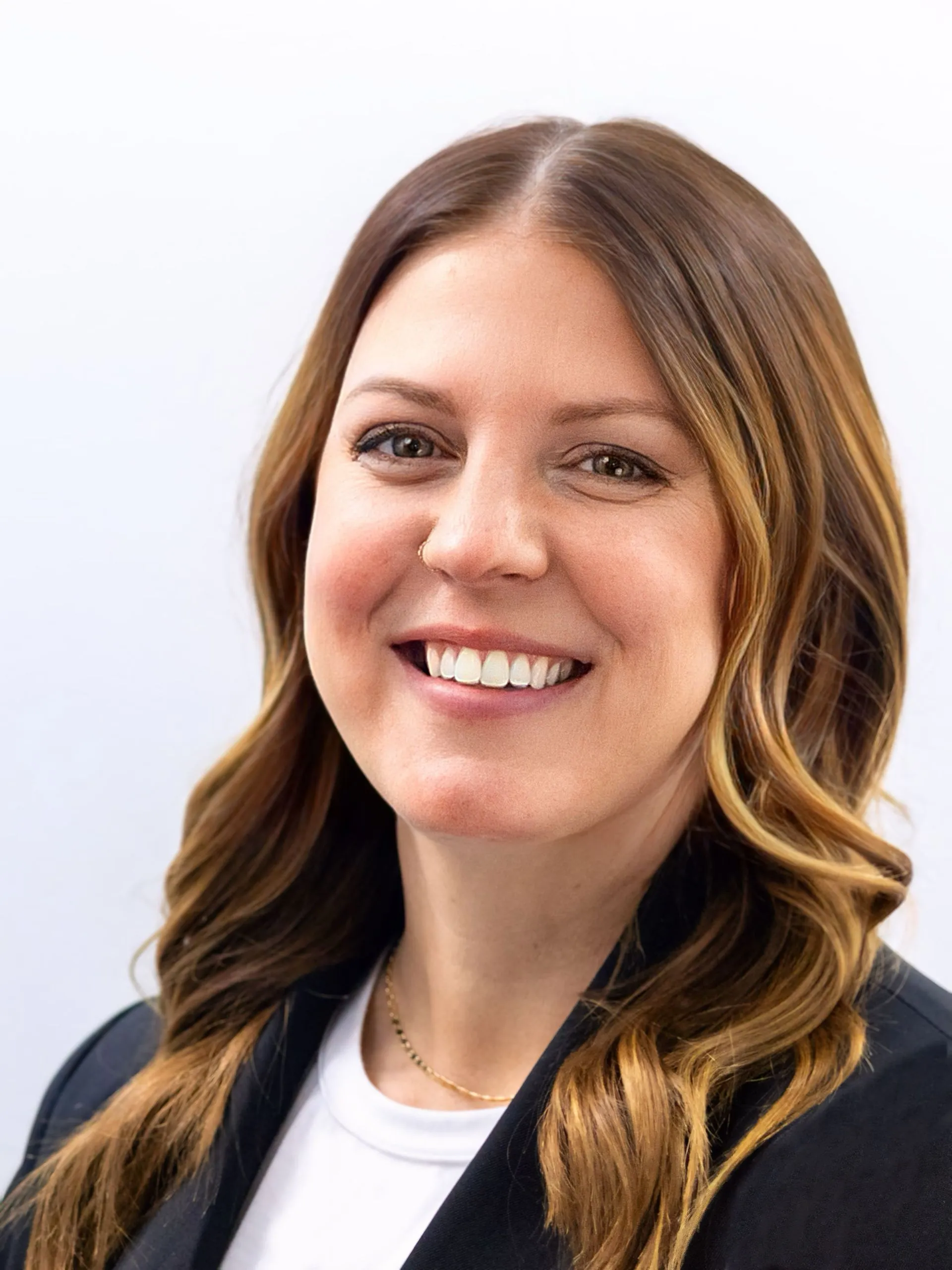 Professional headshot of a smiling woman with wavy brown hair, wearing a black blazer and white top.
