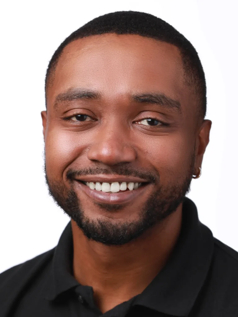 Close-up portrait of a smiling man with short hair, a beard, and a black collared shirt.