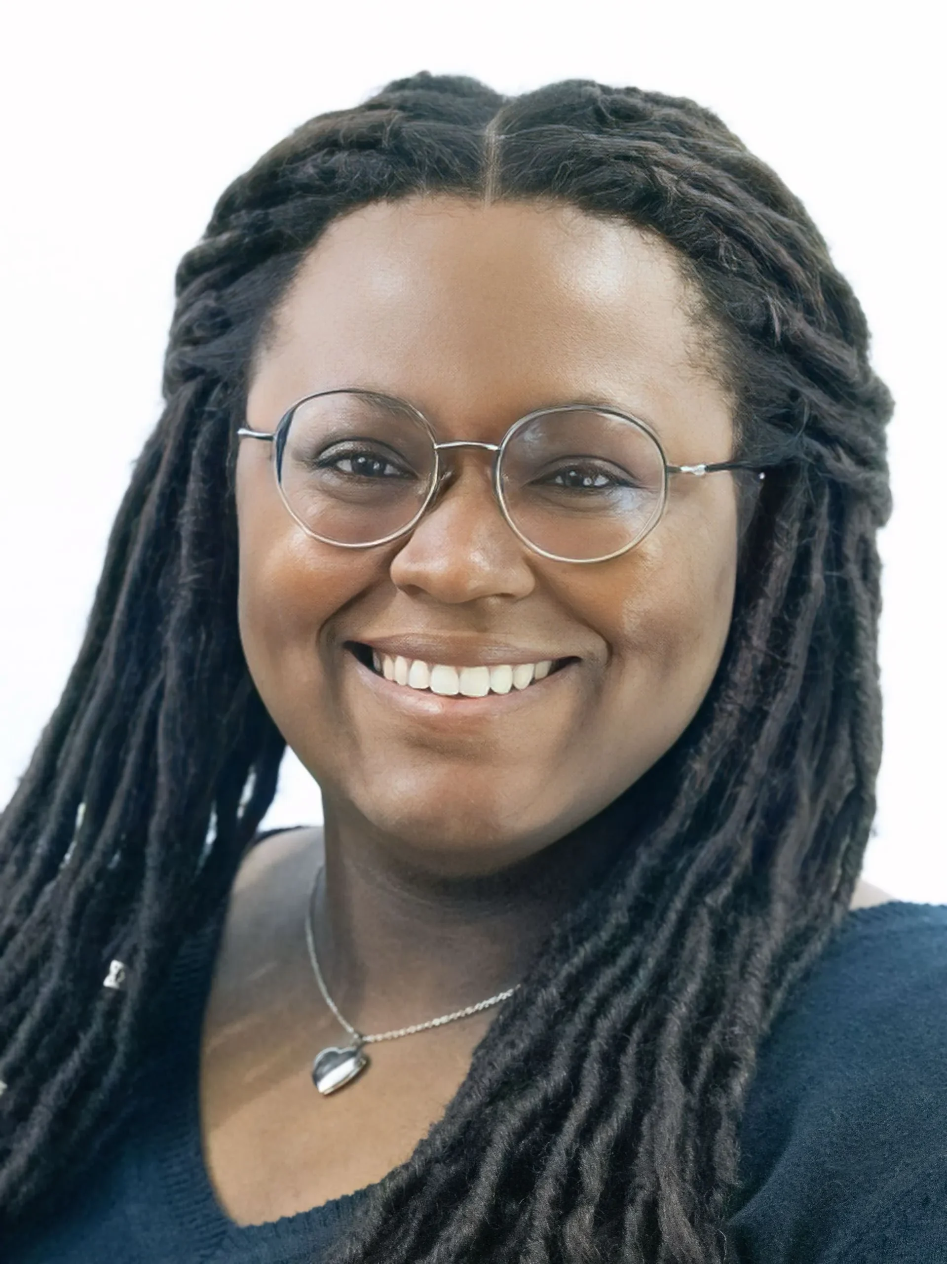 Professional portrait of a smiling woman with long braided hair, round glasses, and a heart-shaped necklace.