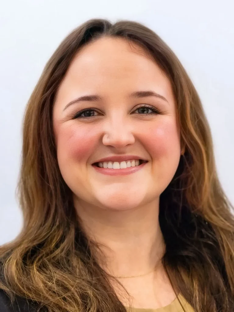 Portrait of a smiling woman with long brown hair against a light background.