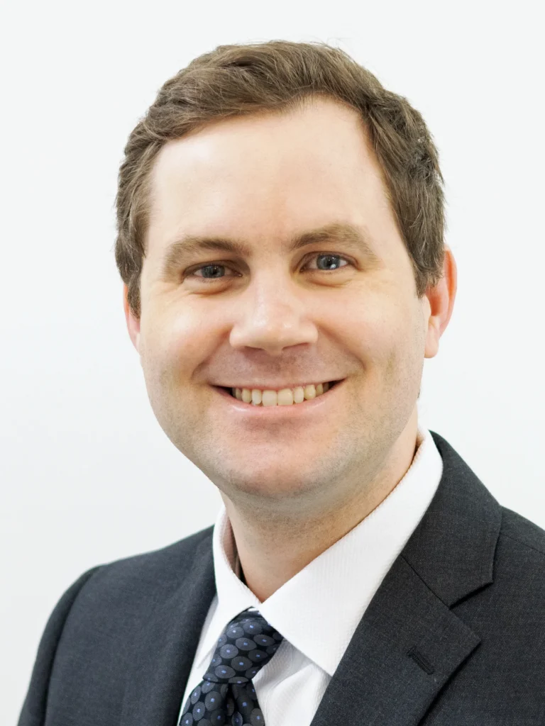 Portrait of a smiling man with light brown hair, wearing a dark suit and patterned tie.